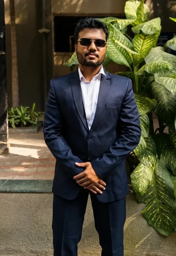 Vandan Dalvi, founder of Whyno, standing in a navy suit and sunglasses beside a leafy plant